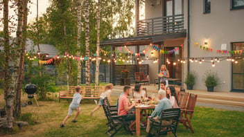 Big Family Garden Party Celebration, Gathered Together at the Table Family, Friends and Children. People are Drinking, Passing Dishes, Joking and Having Fun. Kids Run Around Table.