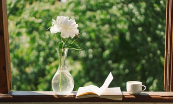 Book, cup coffee and white peonies on a wooden window.