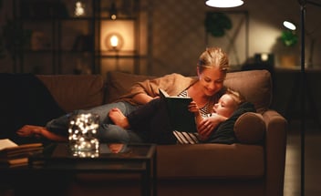 Family before going to bed mother reads to her child son book near a lamp in the evening