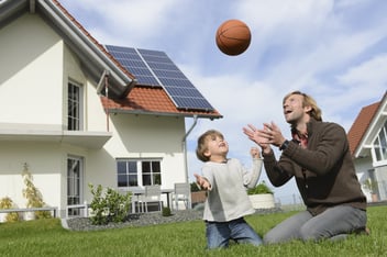 Father throwing ball into air with son on lawn