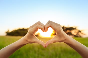 Hand shaped heart against sunset