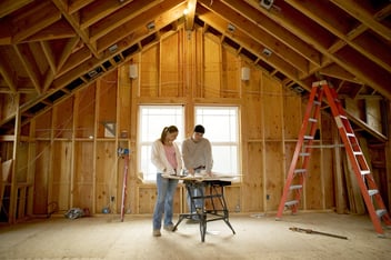 Man and young woman looking at blueprints in house under construction