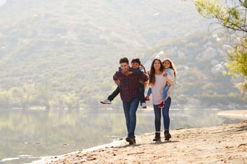 Parents piggybacking their young children by a mountain lake