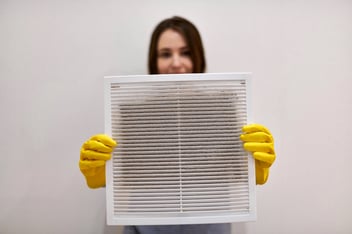 Woman holding dirty and dusty ventilation grille, blurred.