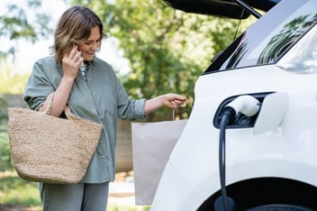 Woman with shopping bag next to a charging electric car