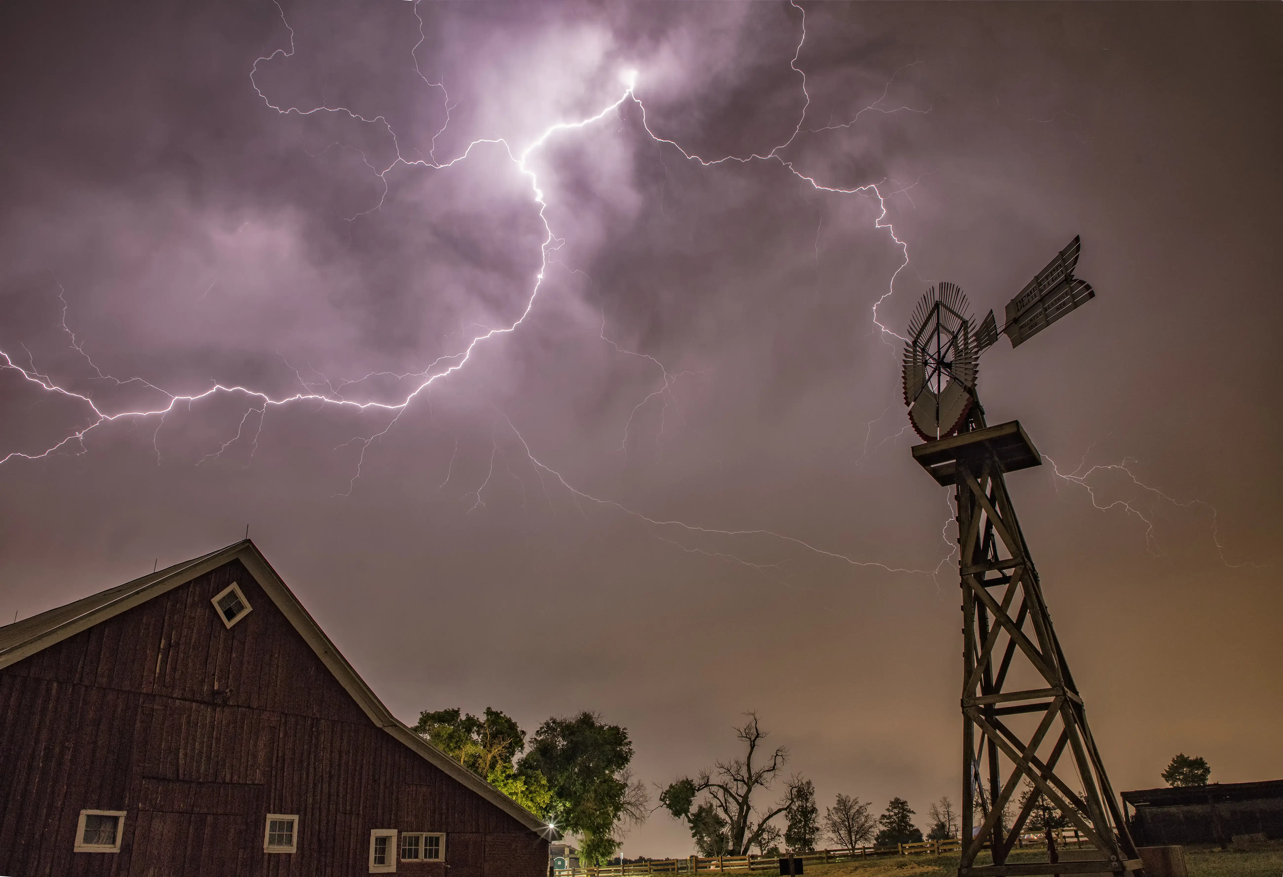 Anvil crawling lightning illuminates an old barn during a thunderstorm