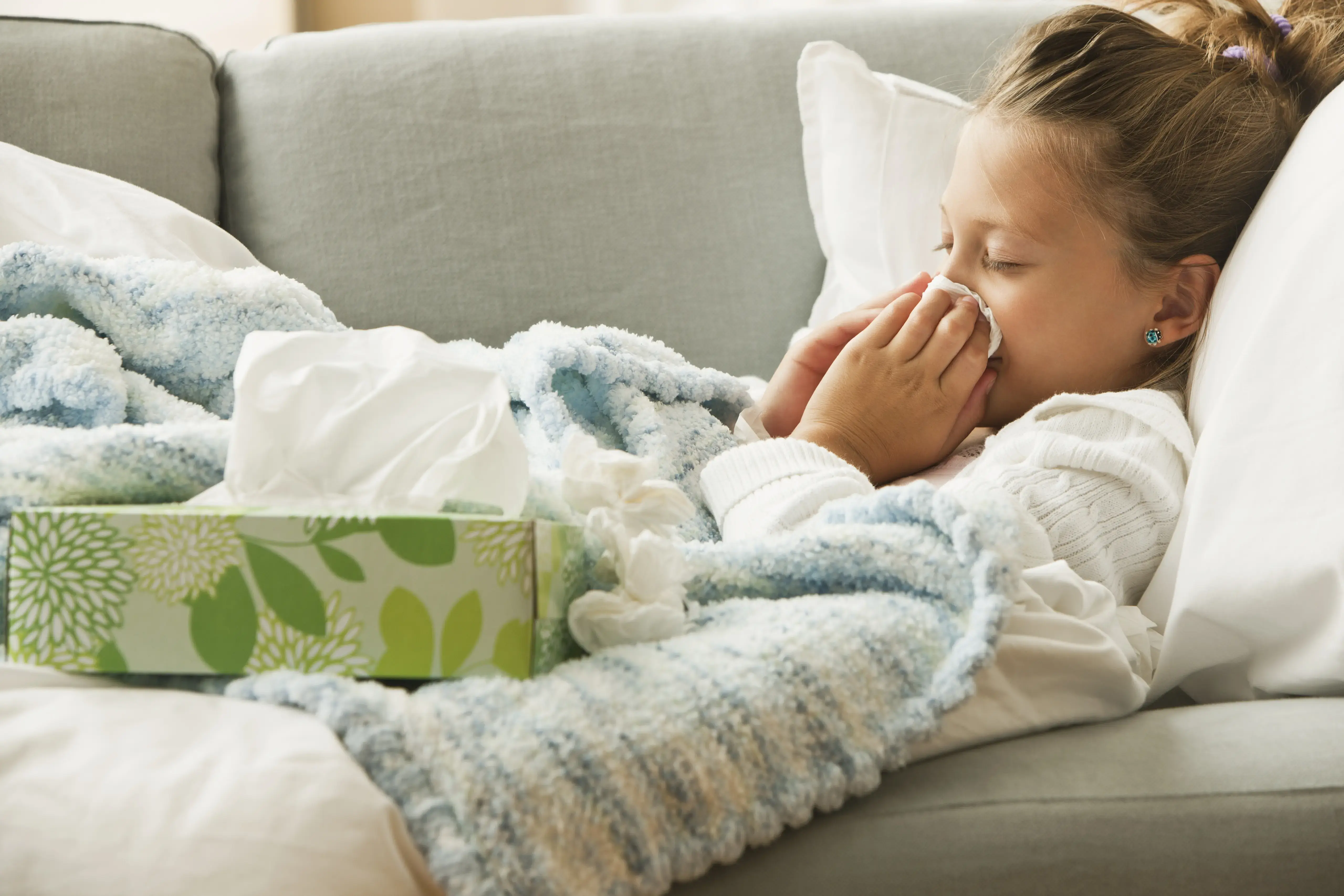 Caucasian girl laying on couch blowing her nose