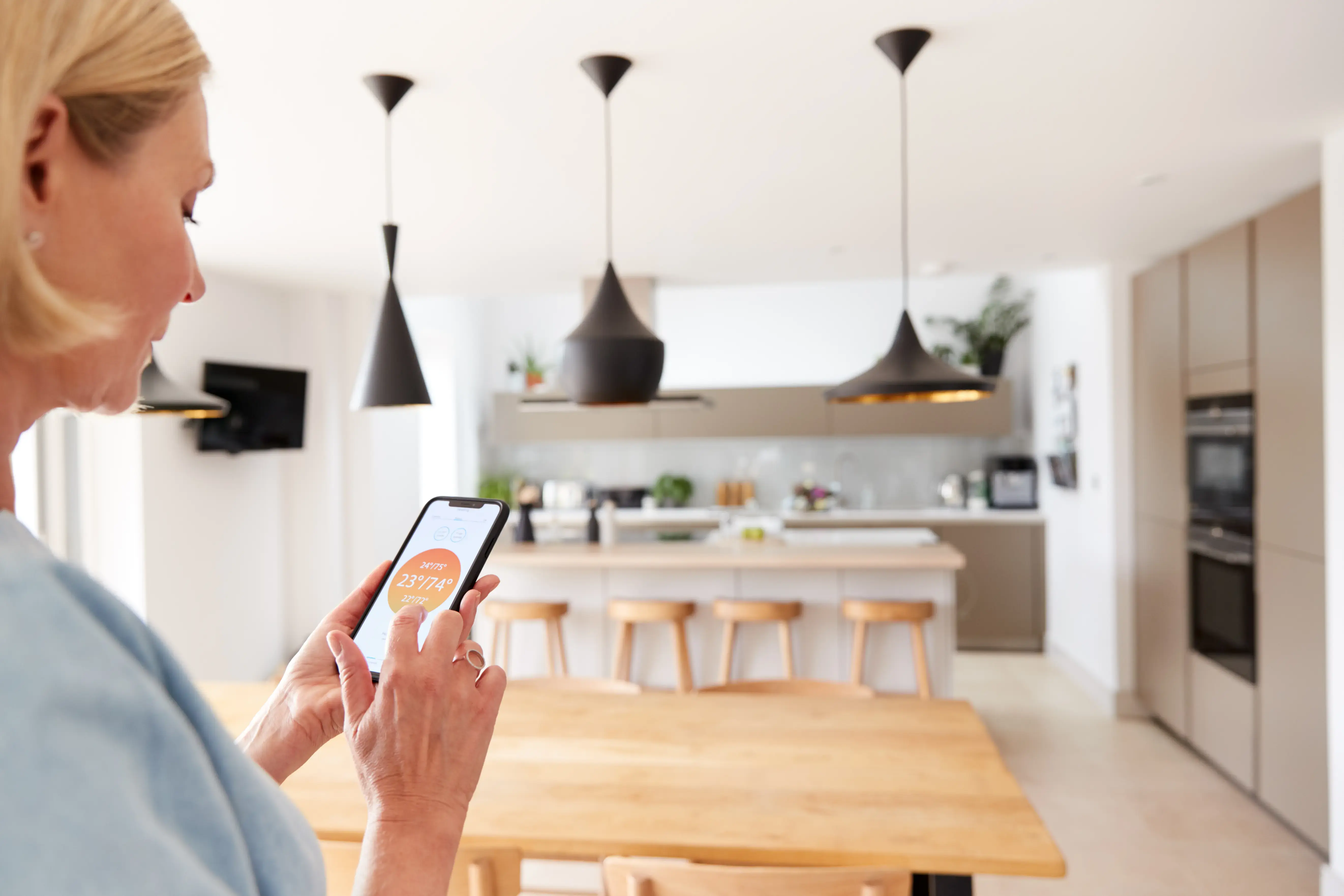 Close Up Of Woman Using App On Smart Phone To Control Central Heating Temperature In House