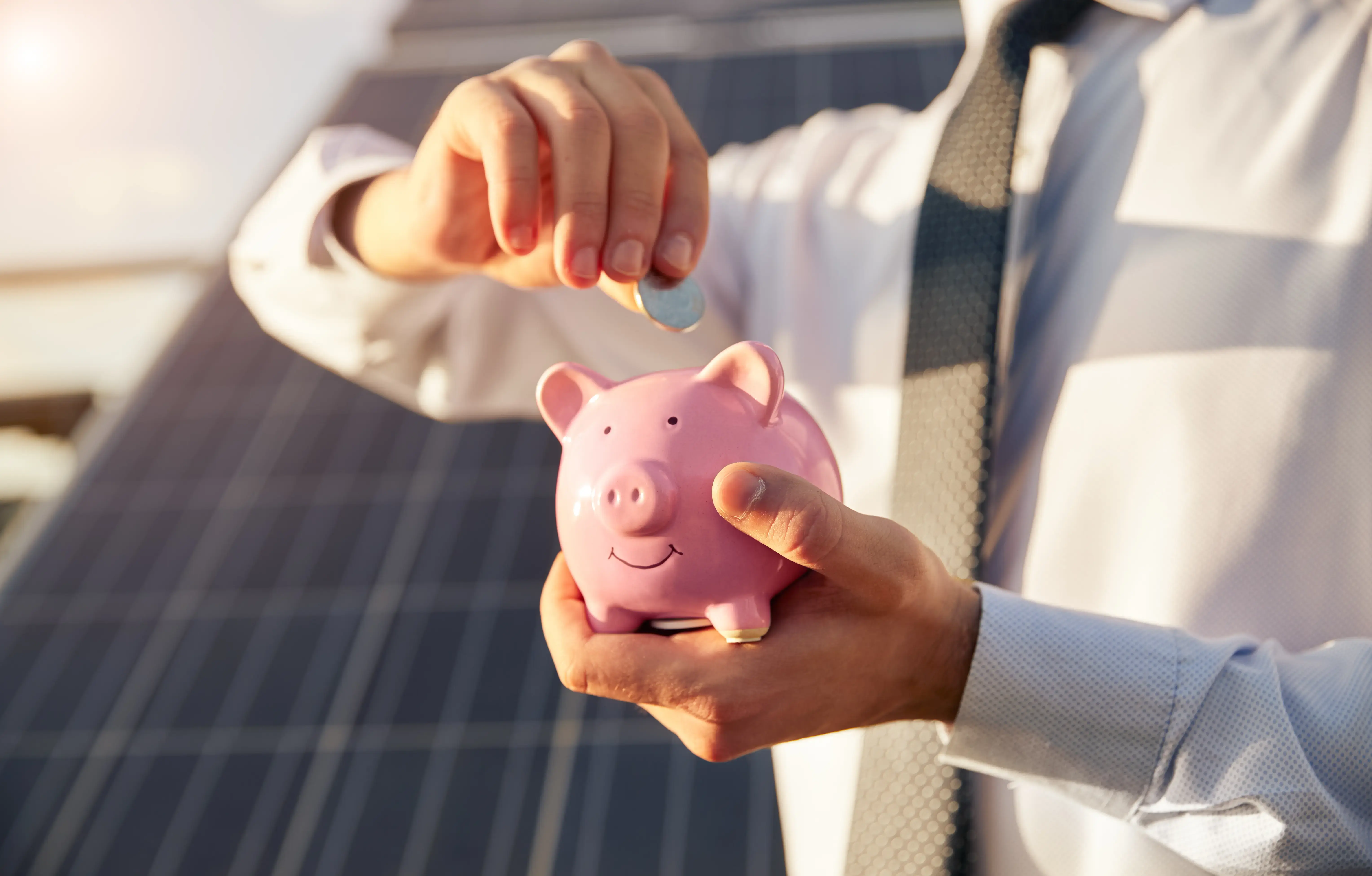 Man putting money into piggy bank near solar panel