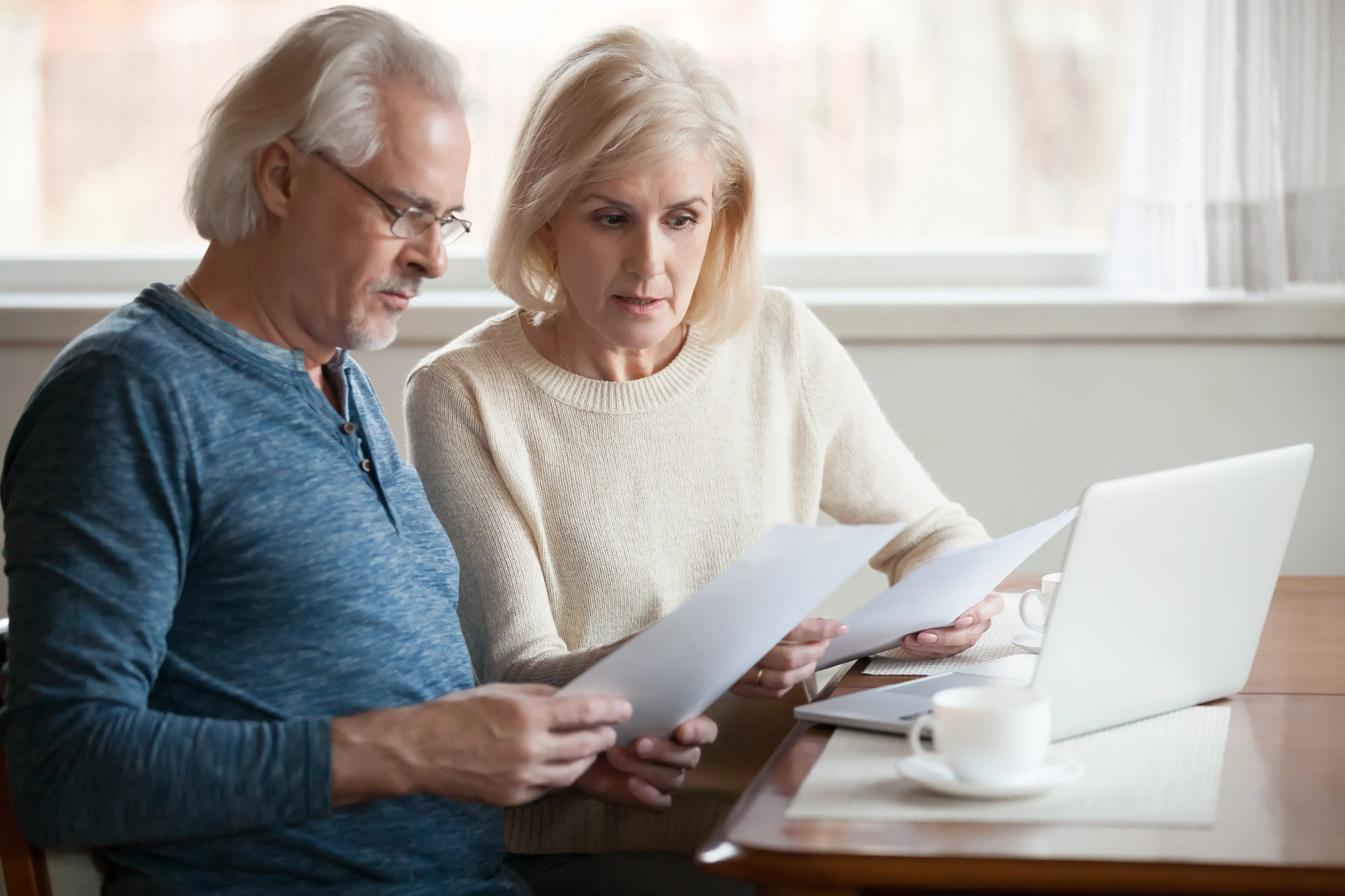 Serious worried senior couple reading documents calculating bills to pay