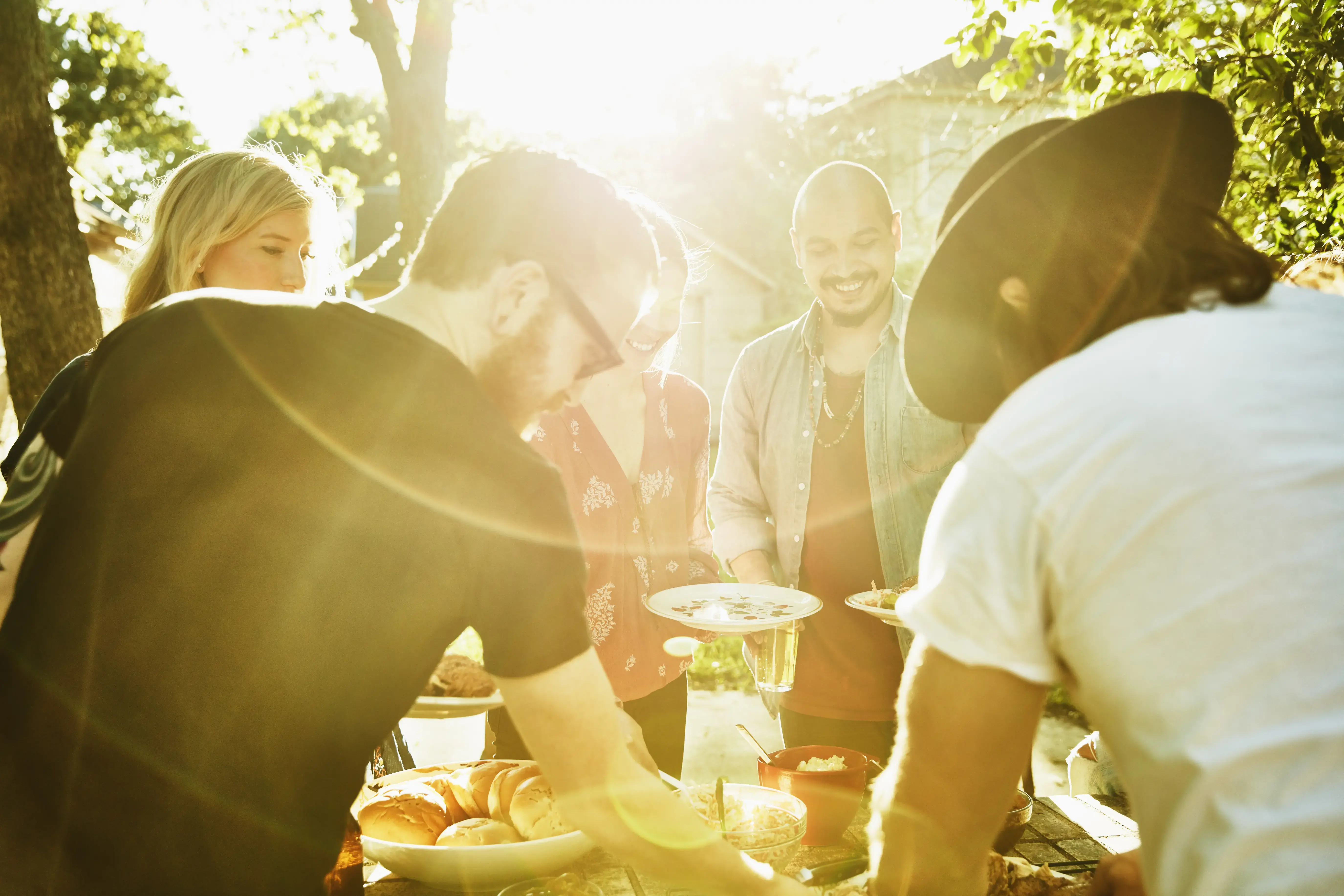 Smiling friends dishing up food in backyard on summer evening