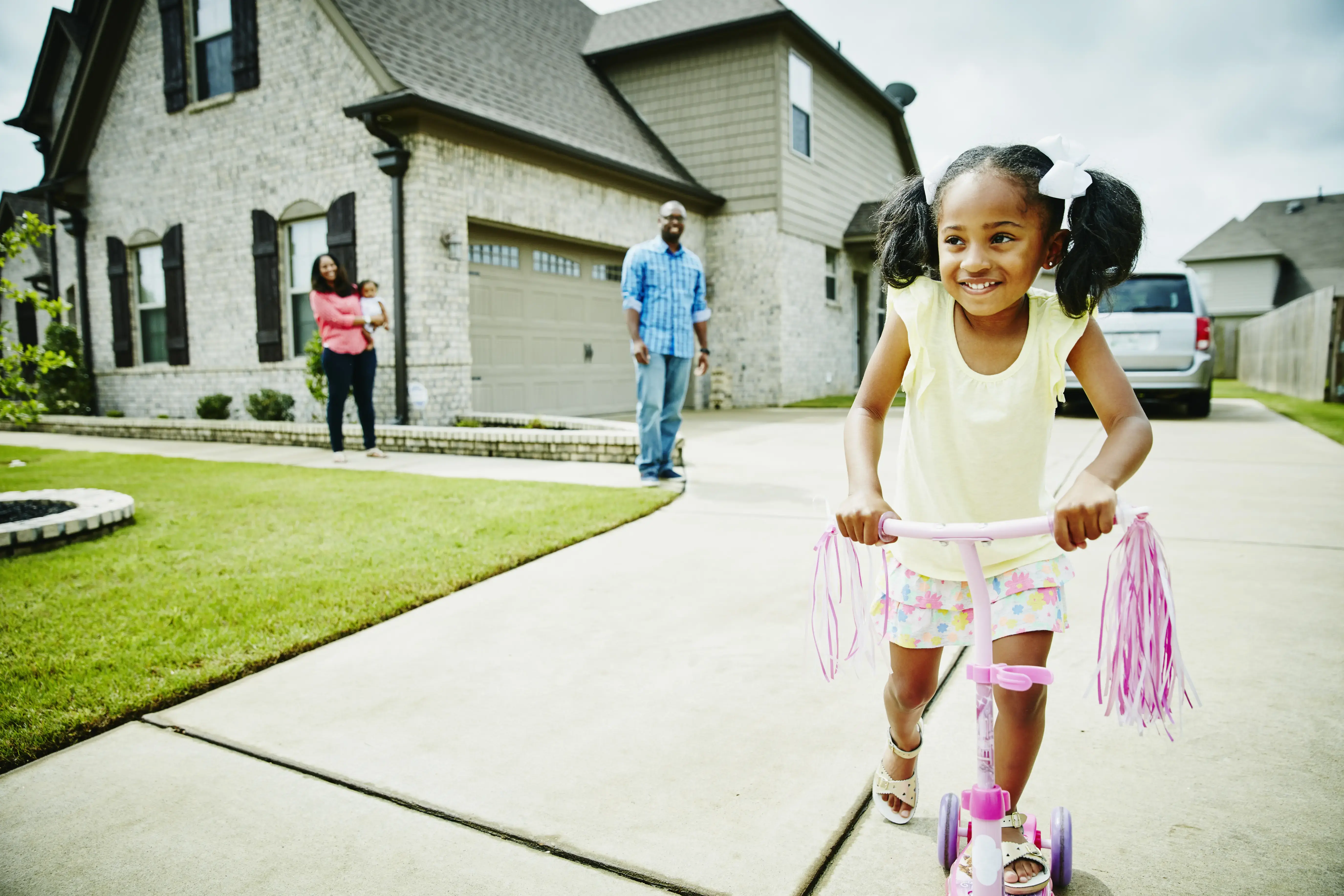 Smiling young girl riding scooter in driveway