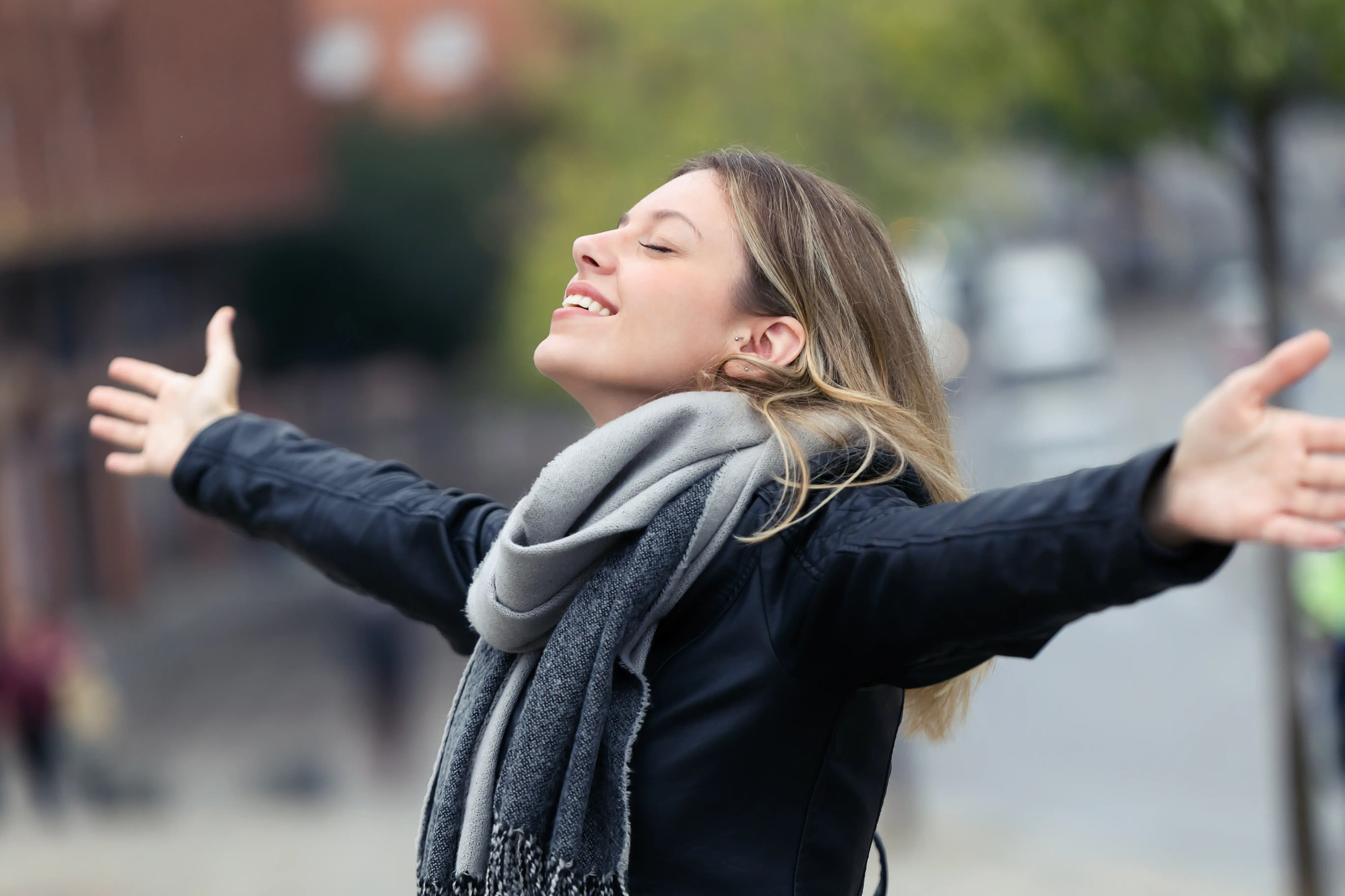 Smiling young woman breathing fresh air and raising arms in the city.