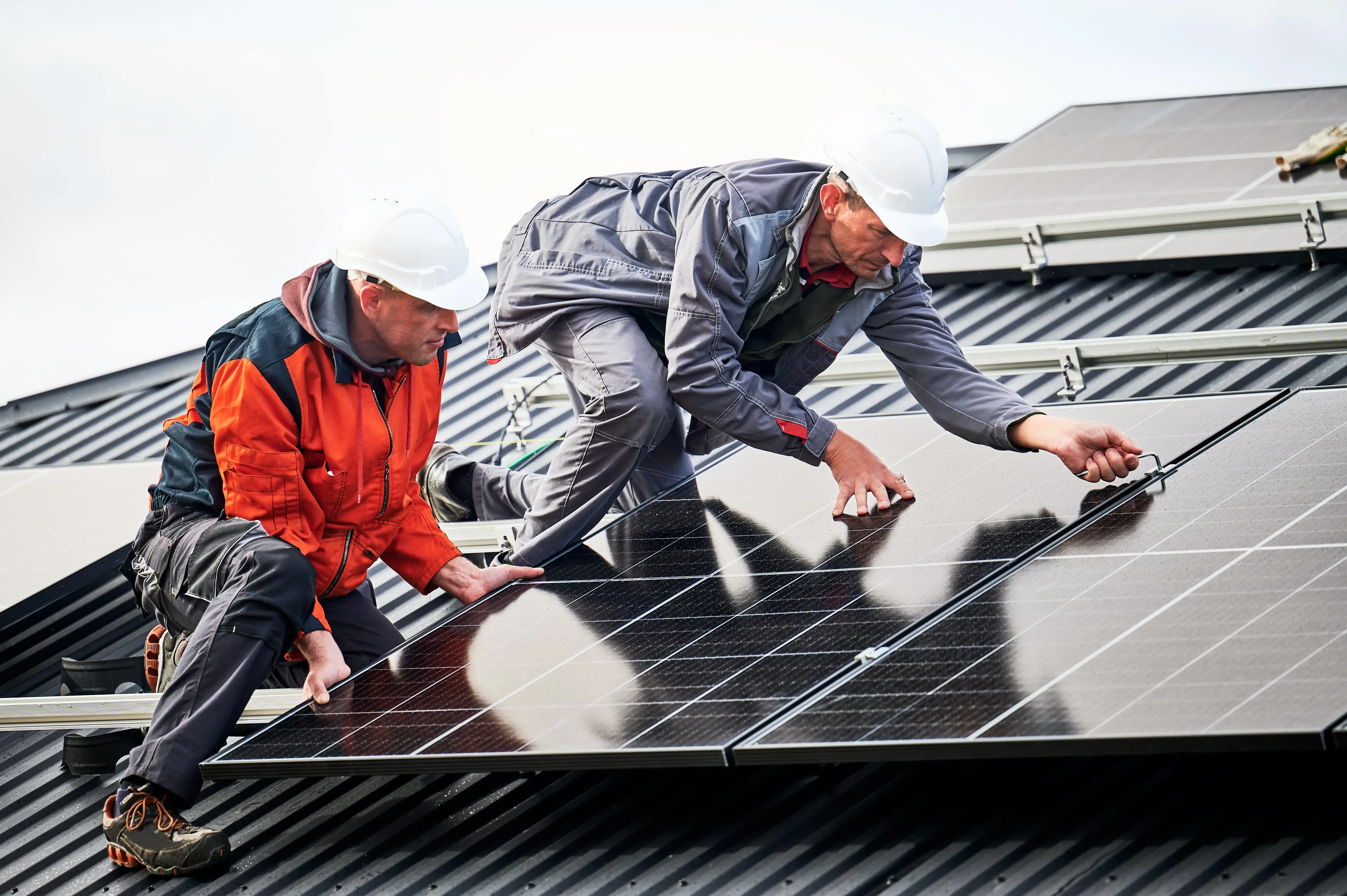 Technicians installing photovoltaic solar panels on roof of house.