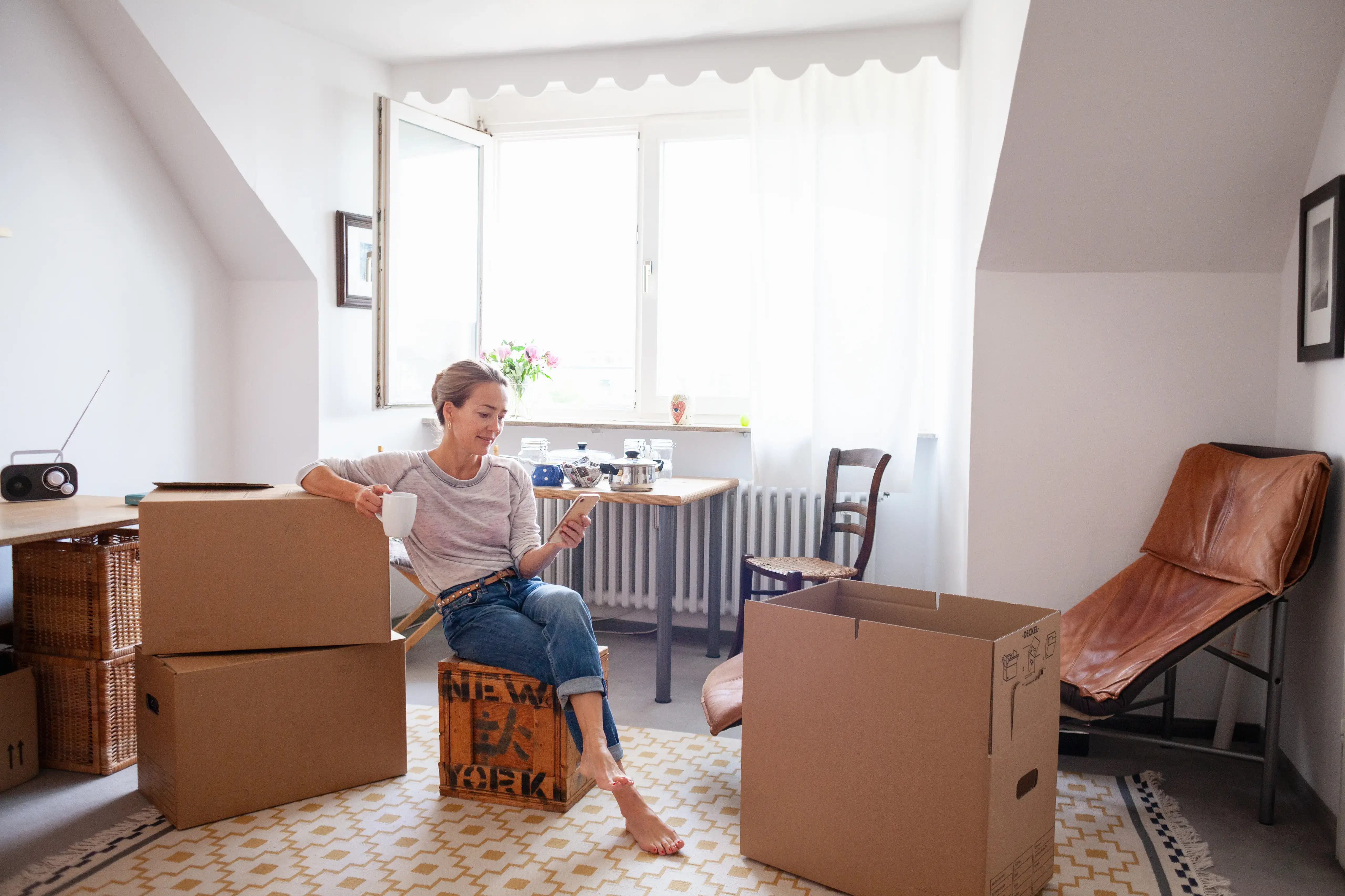 Woman taking a coffee break while moving house, text messaging on mobile phone