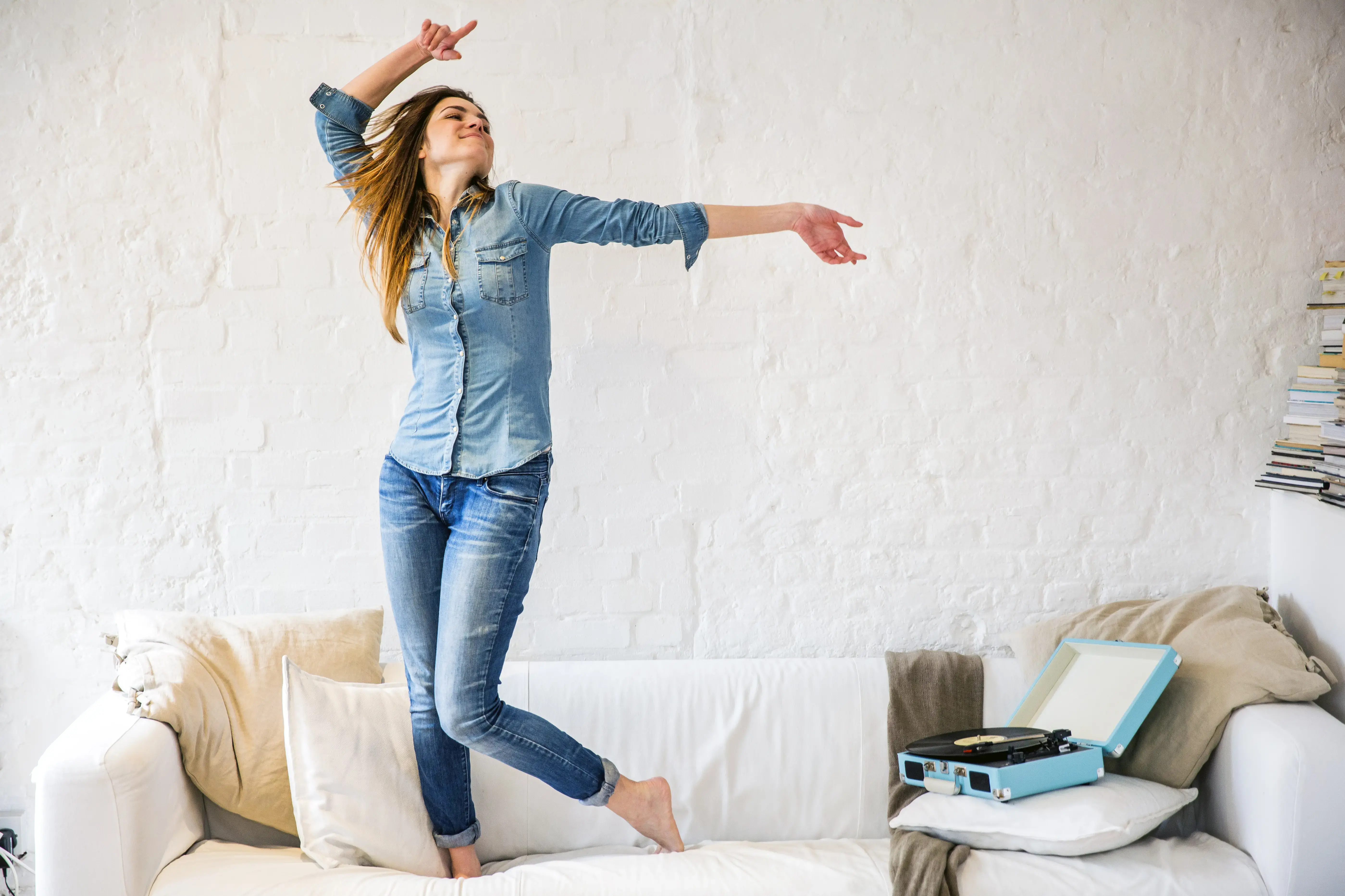 Young woman standing on sofa dancing to vintage record player